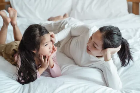 Seorang ibu yang tersenyum sambil mendengarkan penjelasan anaknya untuk mengajari anak berani jujur