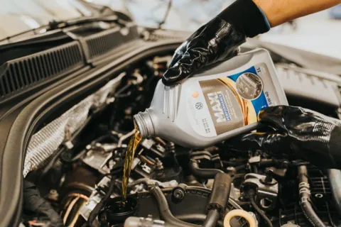 Mekanik menuangkan cairan pelumas untuk menunjukkan perbedaan oli mineral dan sintetik pada mesin mobil