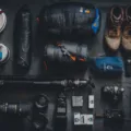 Perlengkapan traveler wajib bawa seperti paspor, kamera, kacamata, dan botol minum di atas meja kayu