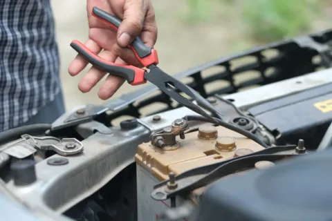 Mekanik sedang memeriksa tanda aki motor lemah menggunakan voltmeter di bengkel
